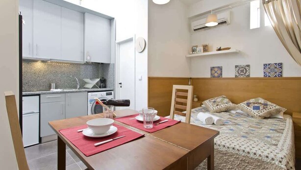 Une pièce de taille modeste comprenant un coin cuisine, une table à manger mise avec des assiettes et des verres, et un lit avec une couette.