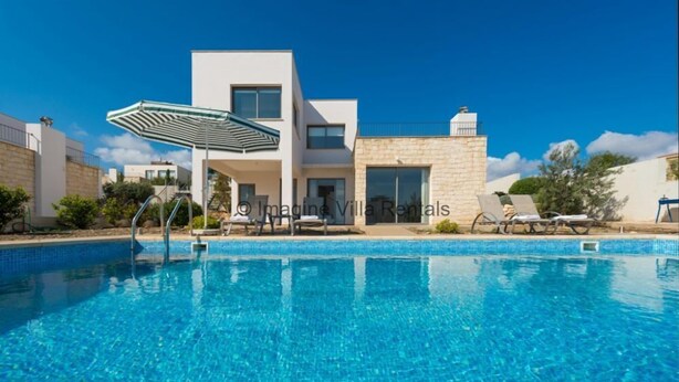 A modern villa with a swimming pool, a covered outdoor seating area, and a stone facade.