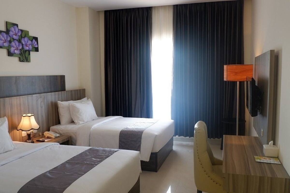 A hotel room with two beds, a desk, a chair, a lamp, a TV, and a painting on the wall.