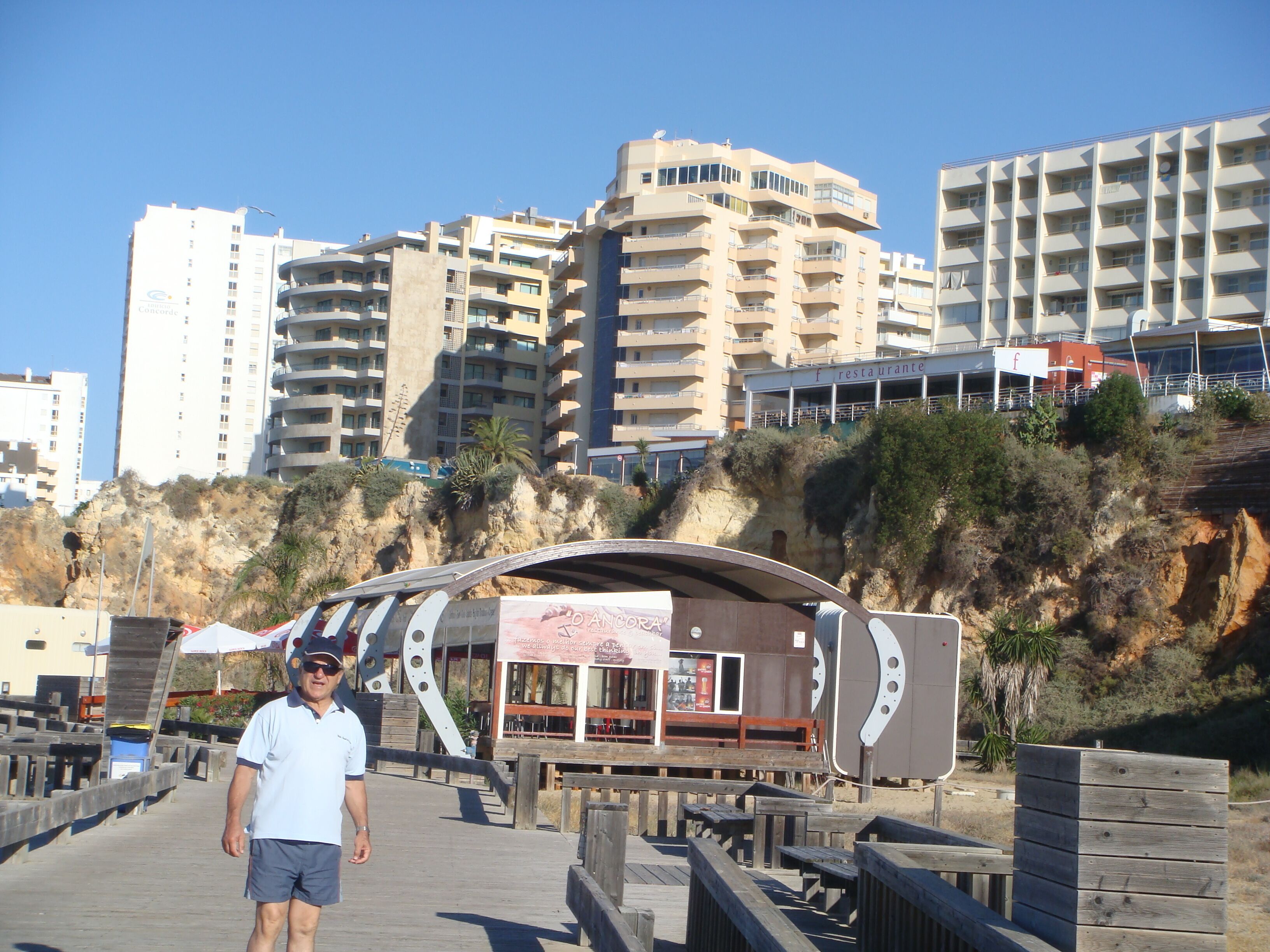 Un hombre caminando sobre una pasarela de madera, con un restaurante al fondo.
