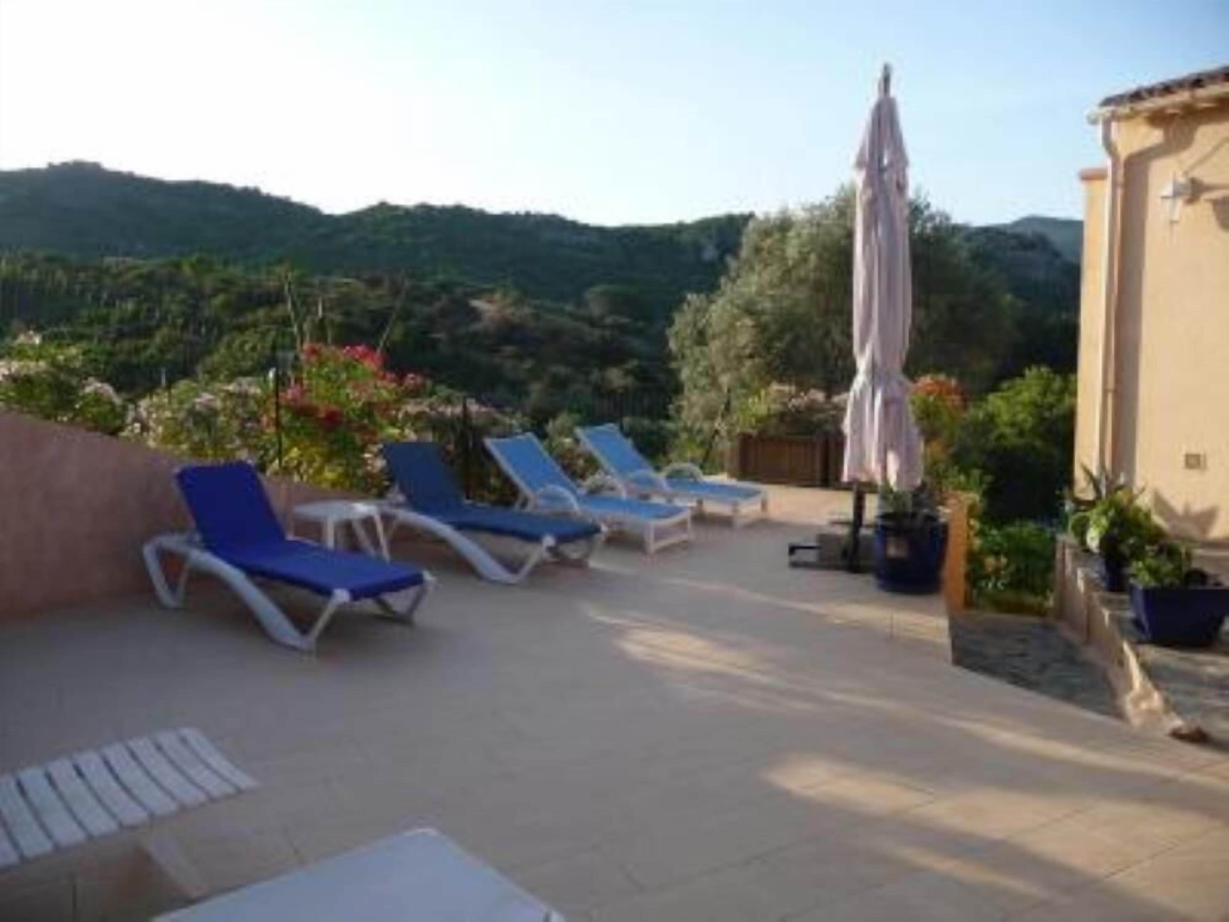 A terrace with lounge chairs and a large umbrella, overlooking a mountainous landscape.