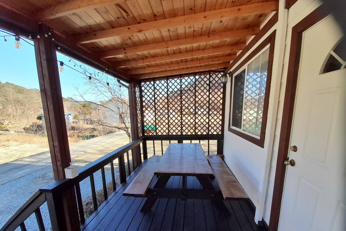 A covered outdoor area with a wooden bench and a door.