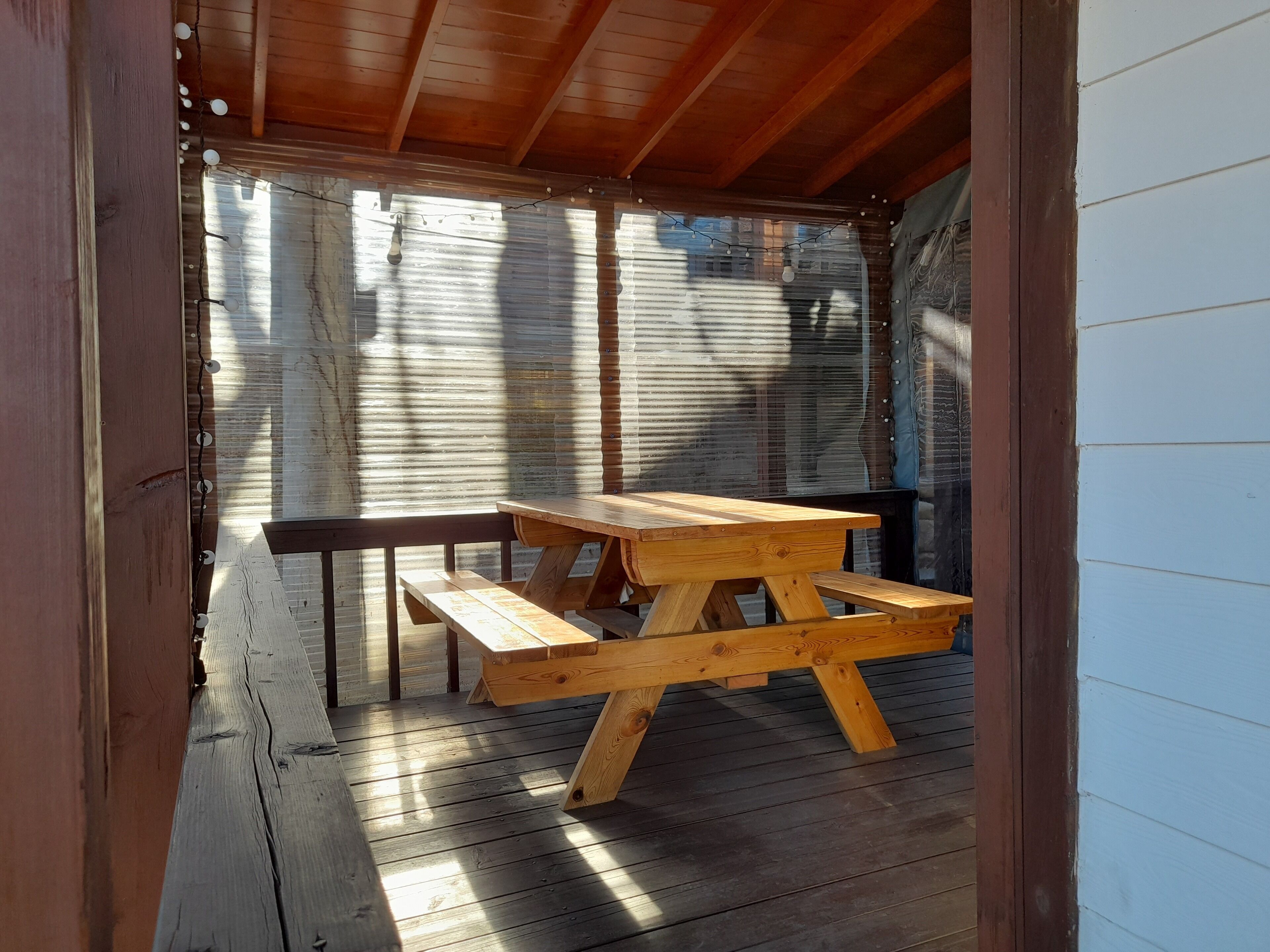 A wooden picnic table with benches in a covered outdoor area with wooden beams and corrugated metal walls.