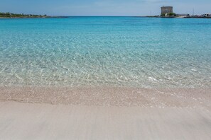 Une plage à l’eau turquoise et limpide, un rivage sablonneux et, au loin, une structure qui ressemble à une tour.