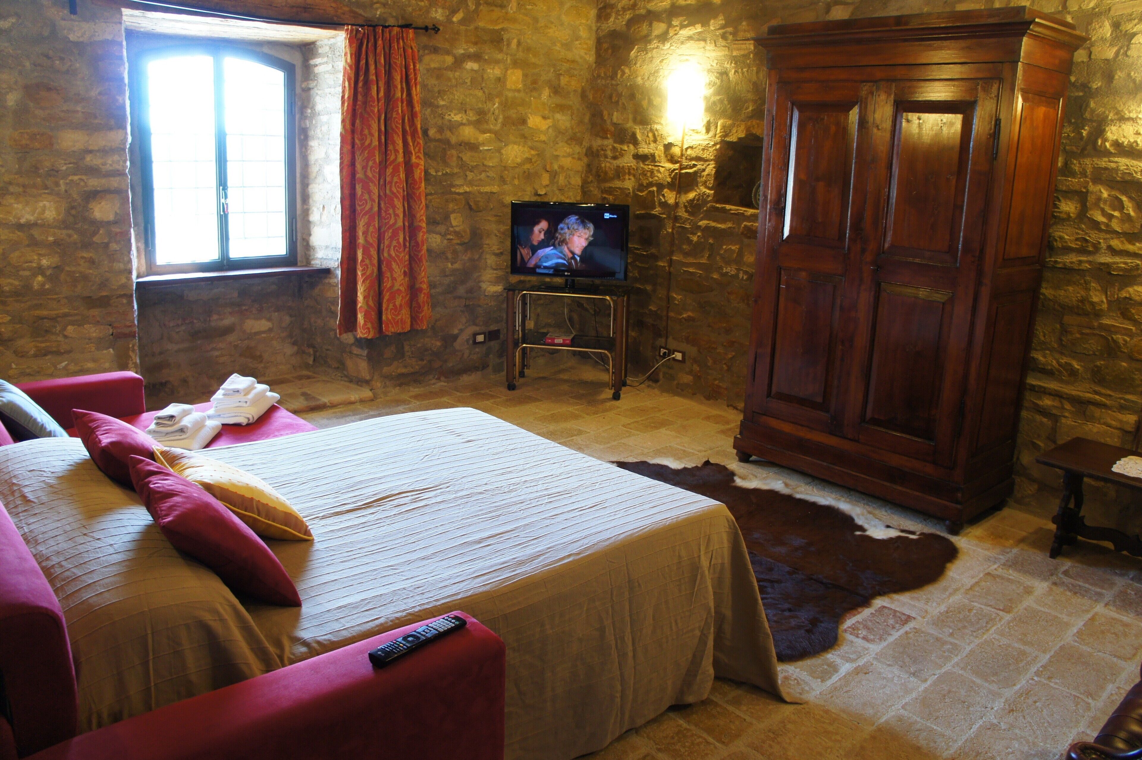 A room with a bed, a television on a stand, a wardrobe, and a stone wall.