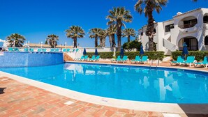 Una piscina con baldosas azules, rodeada de palmeras y sillas de descanso.