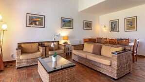 Una sala de estar acogedora con muebles de mimbre, una mesita de centro y cuadros en las paredes.