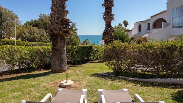 Un jardín con dos sillones de descanso, palmeras y vista al mar.