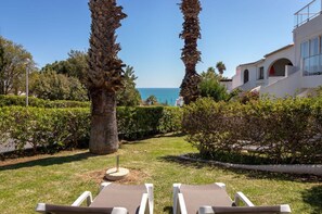 Un giardino con due poltrone, palme e vista sul mare.
