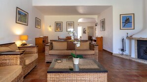 Una sala de estar acogedora con muebles de mimbre, chimenea y cuadros en las paredes.