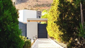 A pathway leading to a building with a modern design, surrounded by greenery and a mountainous backdrop. - Orama Luxury Villa, 4 Bedrooms with Private Pool, Sleeps 8 (Piskopiano)