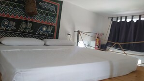 Een kamer met een groot bed, een kleurrijk wandtapijt en een raam met gordijnen.