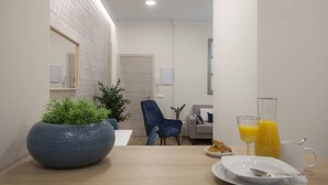 A modern dining area with a wooden table, a blue chair, a sofa, and a large potted plant.