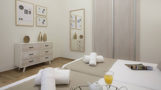 A hotel room with a bed, a bedside table with a glass of orange juice, a white dresser, and a mirror.
