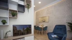 A modern living room with a flat-screen TV, a dining area with a table and chairs, and a blue armchair.