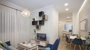 A modern living room with a sofa, a coffee table, a TV, and a dining area with chairs and a table.