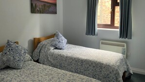 A bedroom with two beds, a radiator, a window with curtains, and a painting on the wall. - Delightful home with balcony overlooking the sea. Easy access, Free car park (MEVAGISSEY, Cornwall)