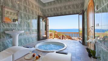 Relax in a spacious bathroom with a hot tub offering ocean views, a pedestal sink, and a seating area with a table and chairs.