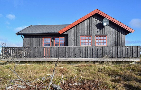 Eine Holzhütte mit rotem Dach und zwei Fenstern mit roten Rahmen.