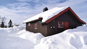 A wooden cabin with a red roof and chimney, surrounded by snow.