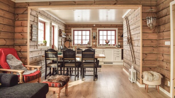 A cozy cabin-style interior with a wooden dining area, a kitchen with a window, and a rustic aesthetic.