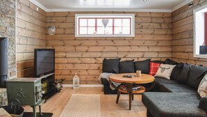 A cozy log cabin interior with a wooden wall, a sofa, a TV, a small table, and a fireplace.