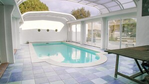 Piscina interna com teto de vidro, cercada por paredes brancas e piso revestido.