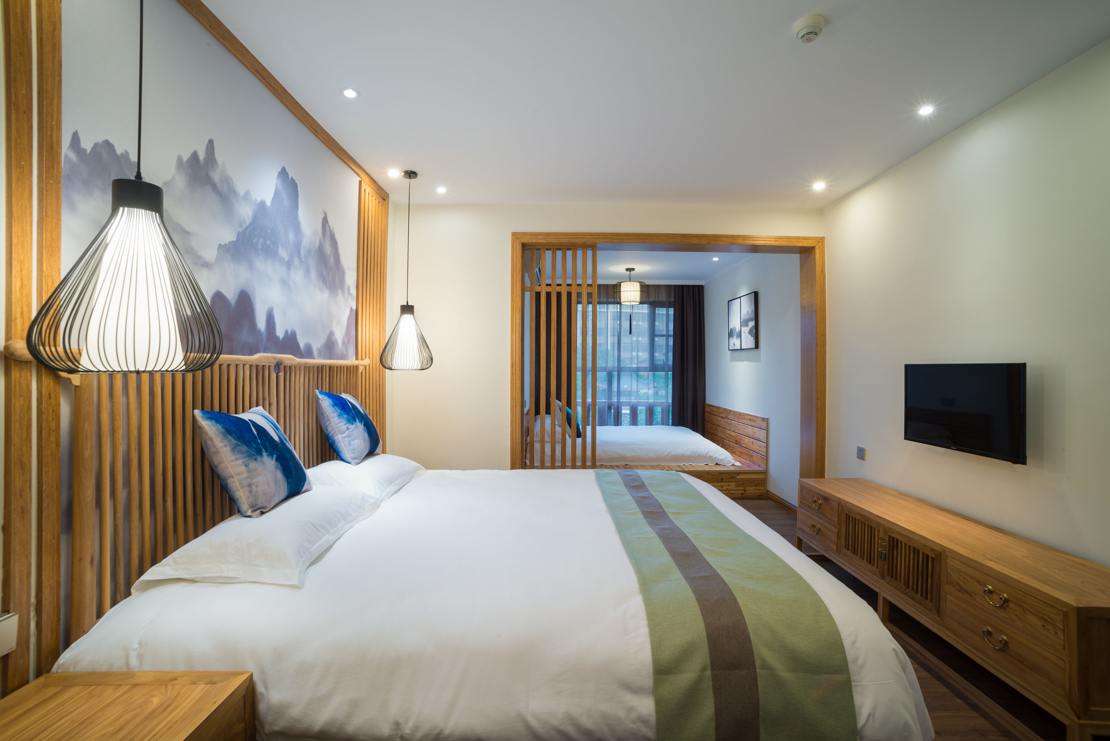 A modern hotel room with a large bed, wooden headboard, and a TV mounted on the wall.