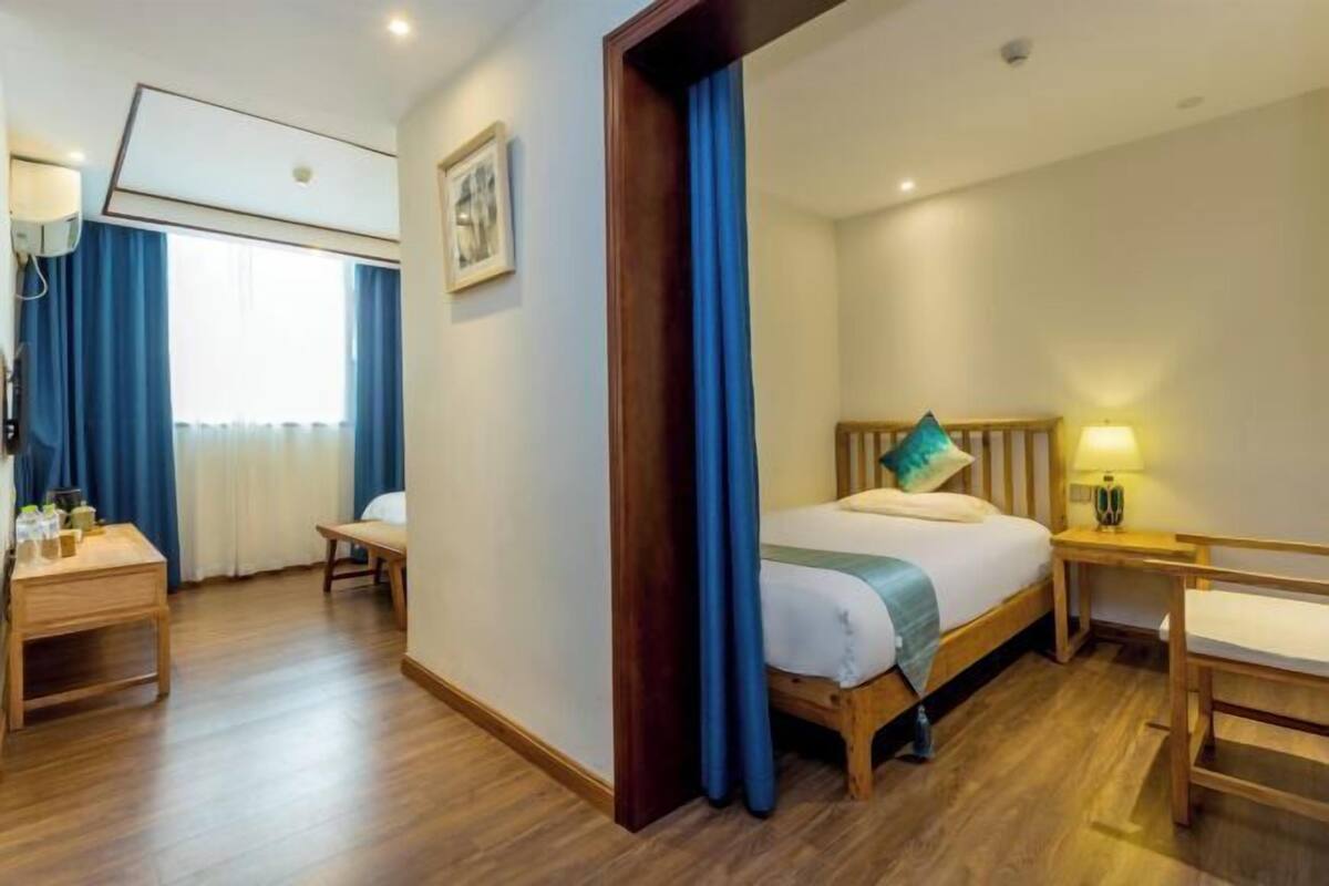 A hotel room with a bed, bedside table, chair, and a window with curtains.