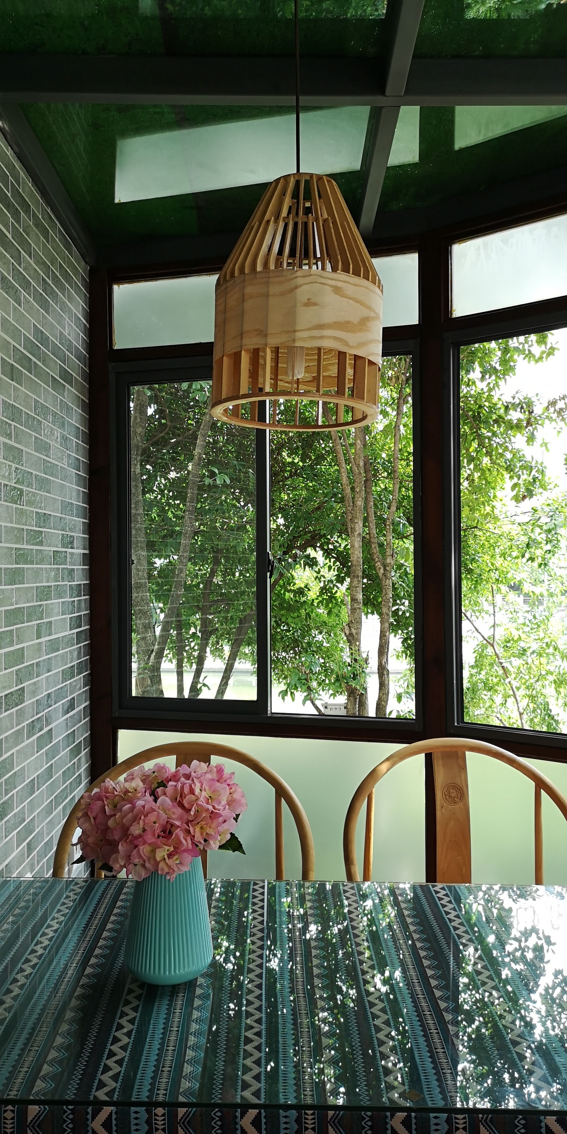 Un comedor con una mesa, sillas, una lámpara colgante y un ventanal con vistas a árboles.