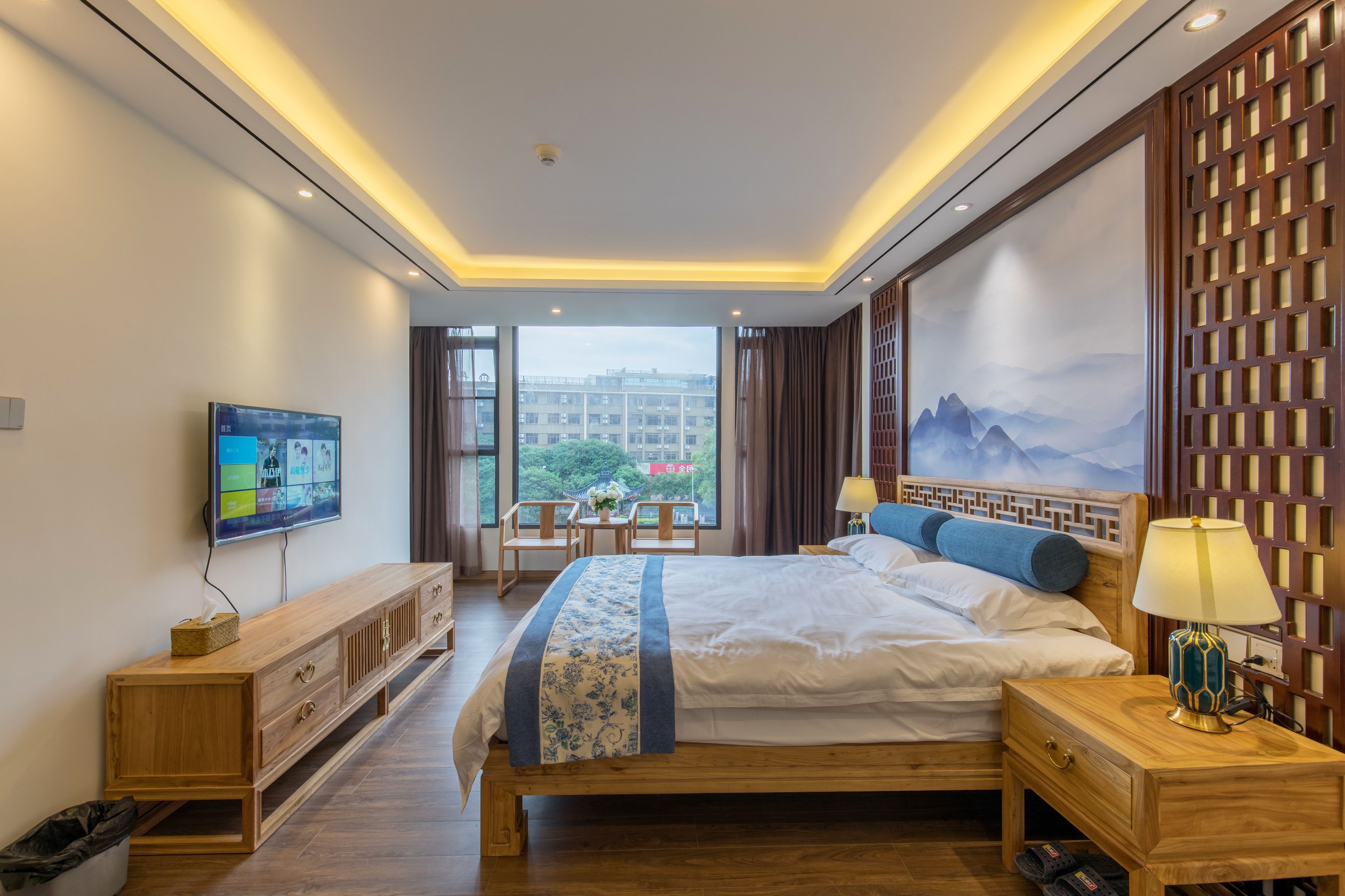 Une chambre d’hôtel moderne avec un grand lit, une télévision, une table de chevet en bois et une vue sur la ville.