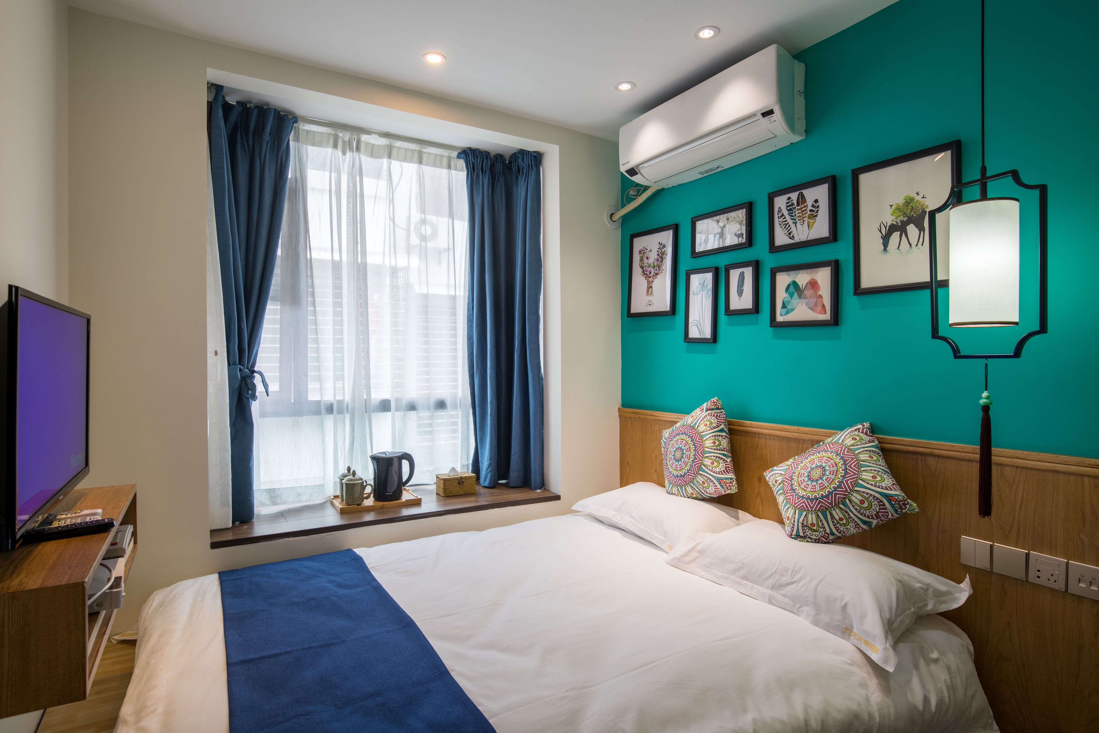 A hotel room with a large bed, a television, a window with curtains, and a wall with framed artwork.