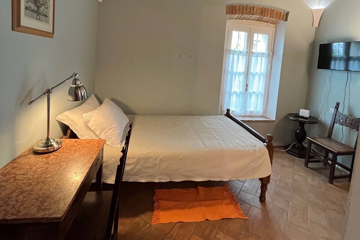 A bedroom with a bed, a desk, a chair, a window, and a television.