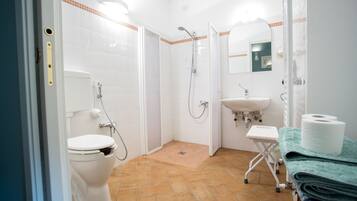 Un baño con inodoro, ducha, lavamanos y un taburete pequeño.
