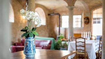 Una stanza con un tavolo di legno, un vaso blu e bianco con fiori bianchi, un divano rosso e un muro in mattoni con finestre ad arco.