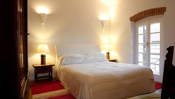 Une chambre avec un grand lit, deux lampes de chevet, une moquette rouge et une fenêtre surmontée d’une arche en briques.