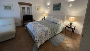 Une chambre à coucher avec un lit, une chaise, un téléviseur et une fenêtre avec des rideaux.
