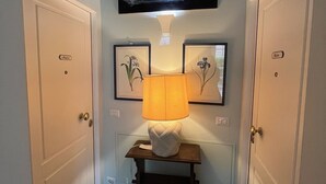 Un couloir avec deux portes, une table avec une lampe, des tableaux encadrés accrochés au mur et un téléviseur fixé au-dessus.