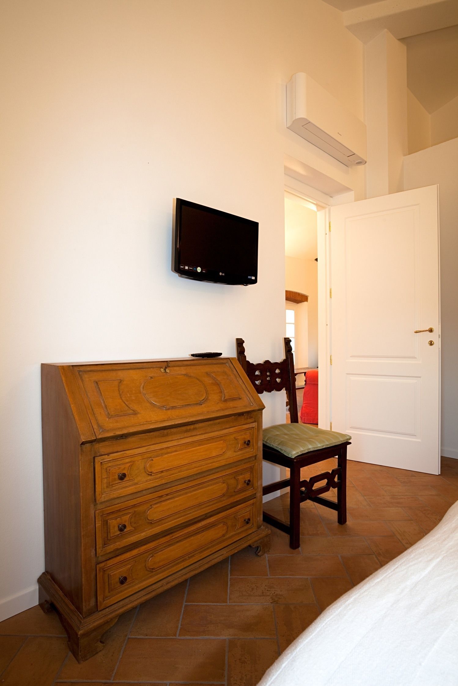A bedroom with a wooden dresser, a television mounted on the wall, and a door leading to another room.
