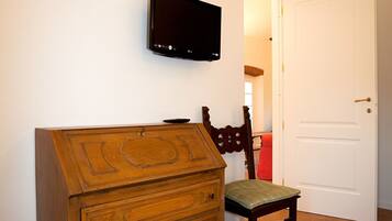 A bedroom with a wooden dresser, a television mounted on the wall, and a door leading to another room.