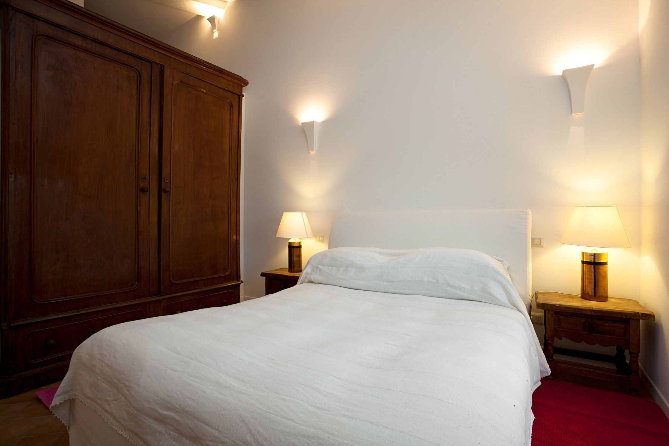 Un letto rifatto con lenzuola bianche, due lampade ai comodini e un armadio in legno.