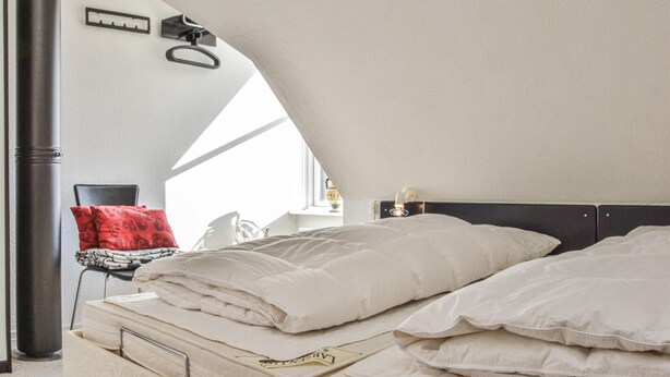 Une chambre à coucher avec un lit, des oreillers, une table de chevet, une lampe et une fenêtre.