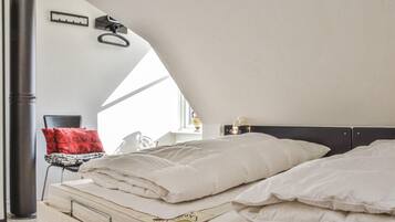 Une chambre à coucher avec un lit, des oreillers, une table de chevet, une lampe et une fenêtre.