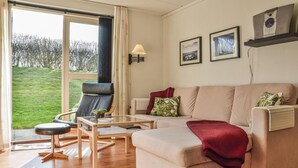 Un salon moderne avec un canapé, un fauteuil et une table basse. Une fenêtre offre une vue sur un paysage verdoyant.