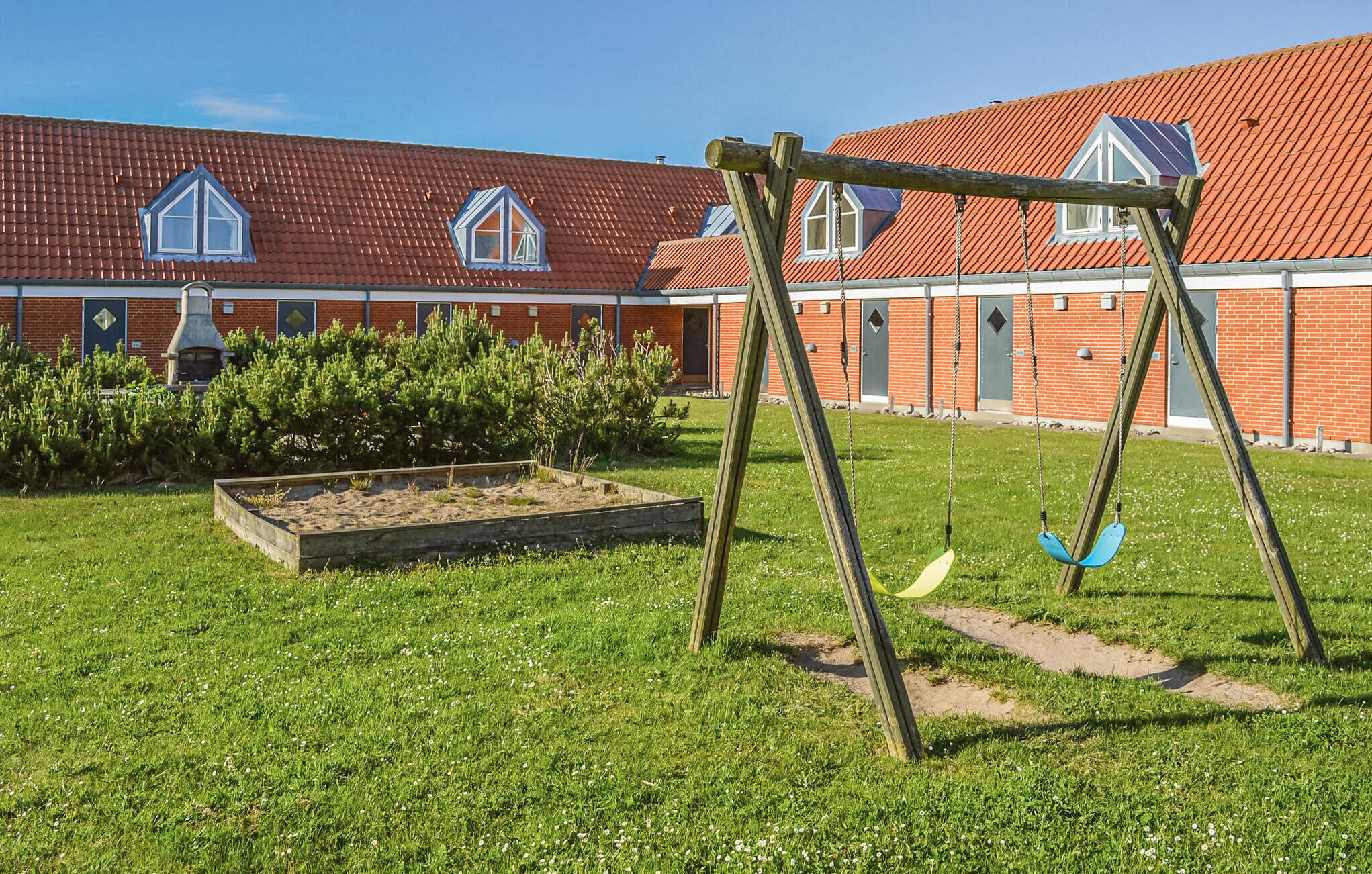 Un terrain de jeux avec des balançoires devant un bâtiment dont le toit est recouvert de tuiles rouges et qui possède des fenêtres.