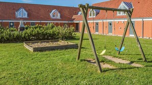 Un terrain de jeux avec des balançoires devant un bâtiment dont le toit est recouvert de tuiles rouges et qui possède des fenêtres.