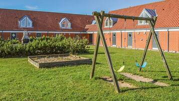 Un terrain de jeux avec des balançoires devant un bâtiment dont le toit est recouvert de tuiles rouges et qui possède des fenêtres.