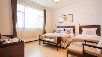 A hotel room with two beds, a wooden desk, and a large window with curtains.