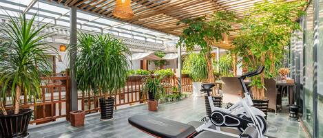 An indoor gym with exercise equipment, potted plants, and a wooden ceiling structure.