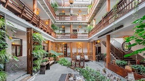 Een meerlaags atrium met houten balustrades, potplanten en een centrale zithoek met tafels en stoelen.